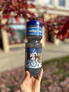 A hand holds up a grey and blue water bottle in front of a tree with red leaves