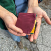 A person is holding a small maroon wallet in their hands, with a small tag that says Fifth Season. The interior of the wallet is colorful, with yellow and green accents visible. 
