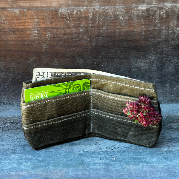 A waxed canvas wallet with a Middlebury Natural Foods Co-op card and a Seedum flower in it, a twenty dollar bill is visible on the top